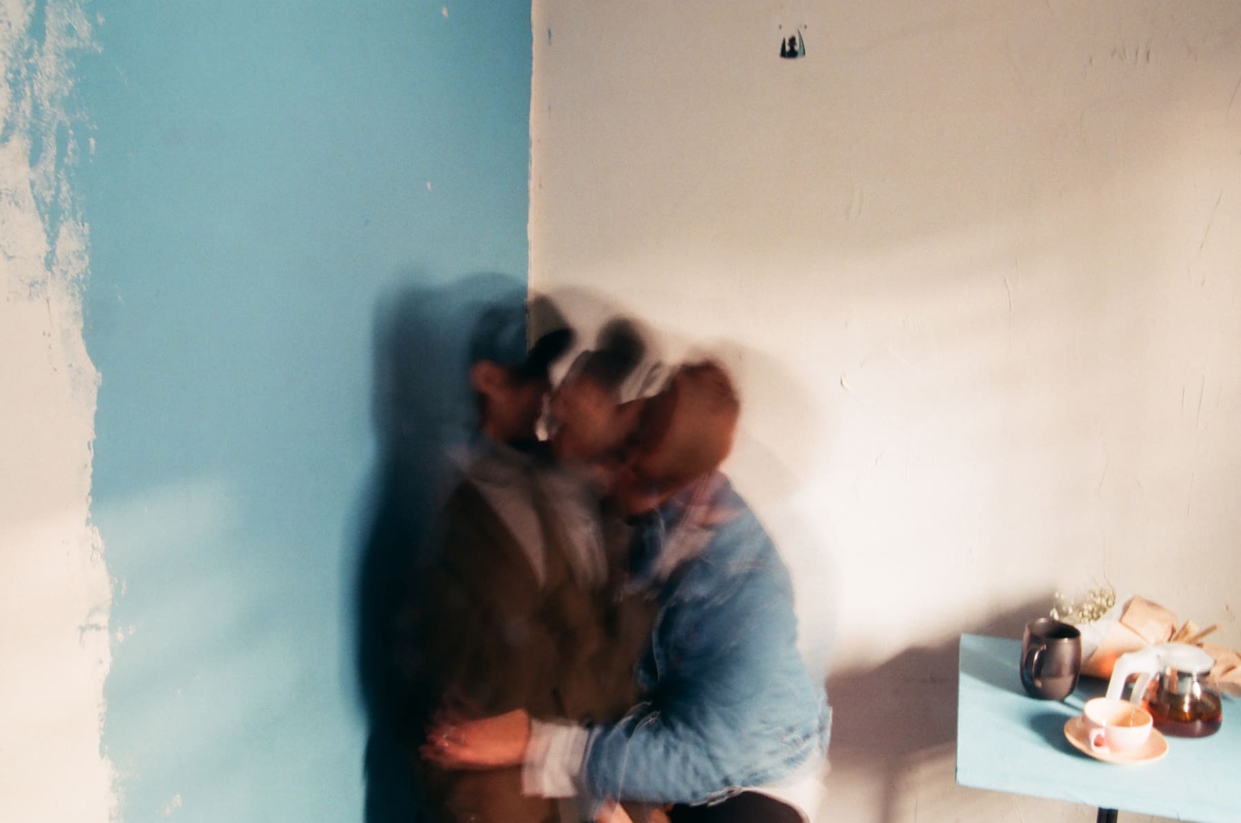 Two people embracing in motion beside a turquoise wall, photographed by Jeon Yoonyoung